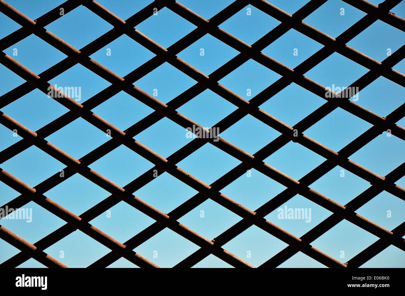 Chainlink Fence Against Blue Sky - Section of a chainlink fence, behind the blue sky as a symbol of captivity and freedom. Stock Photo