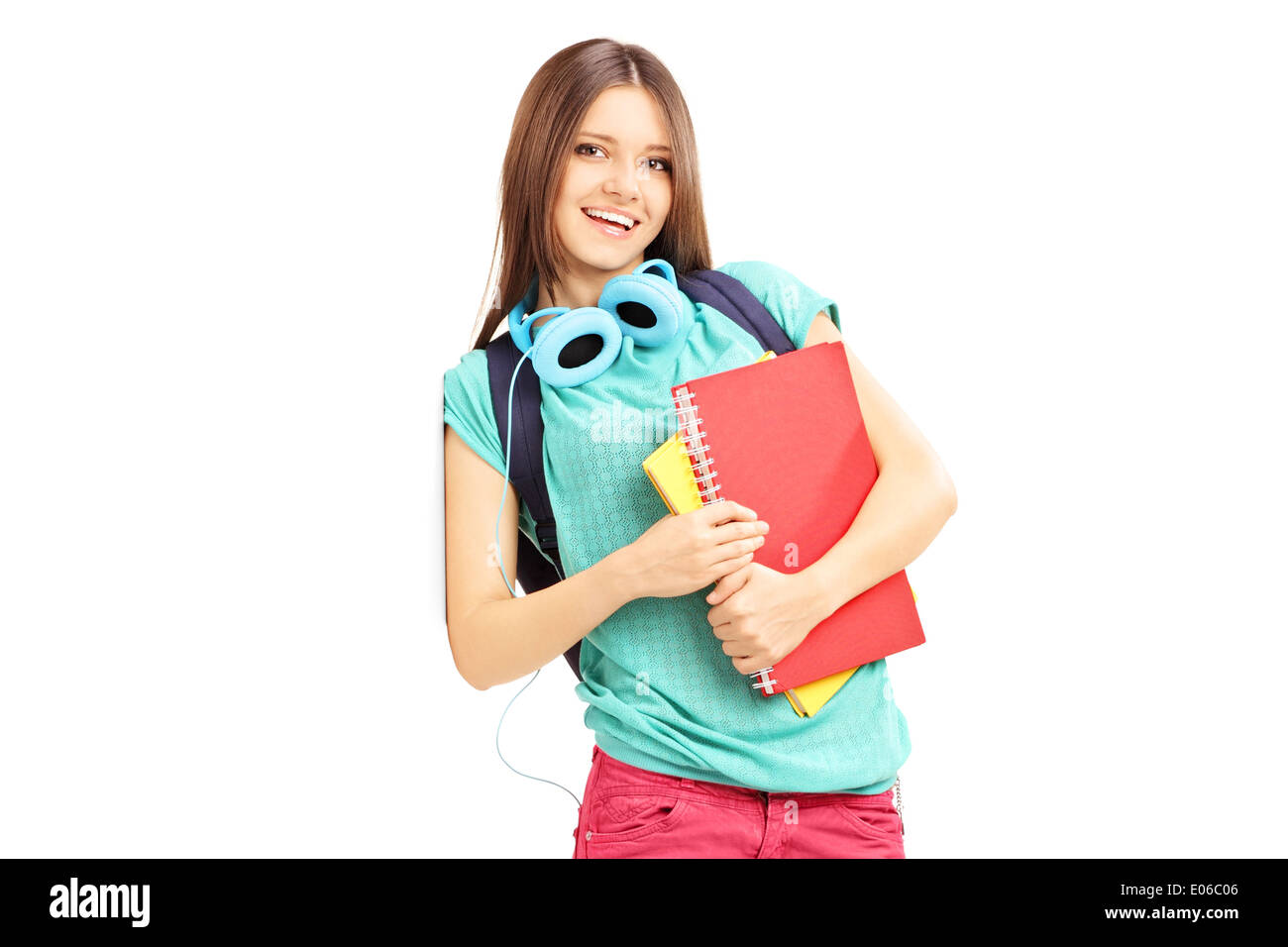 Smiling female with schoolbag and headphones looking at camera and leaning against a wall Stock Photo