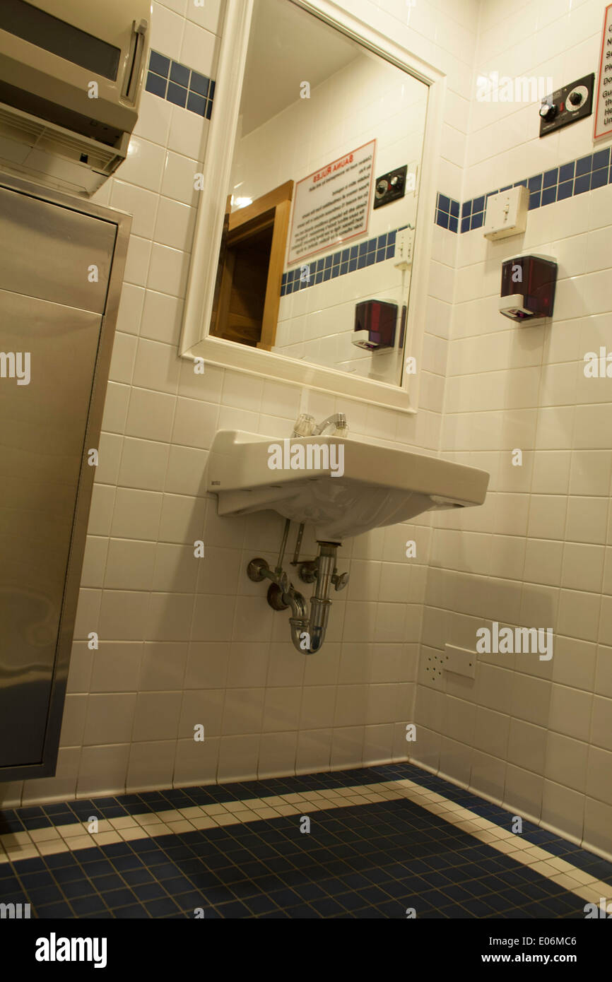 Small tiled public bathroom in a hotel.  Note sauna controls on upper right and in mirror reflection. Stock Photo