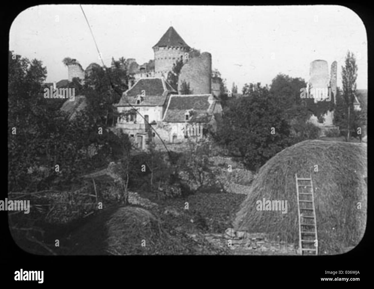 A photograph of a ruined castle with towers, a house, and a haystack ...