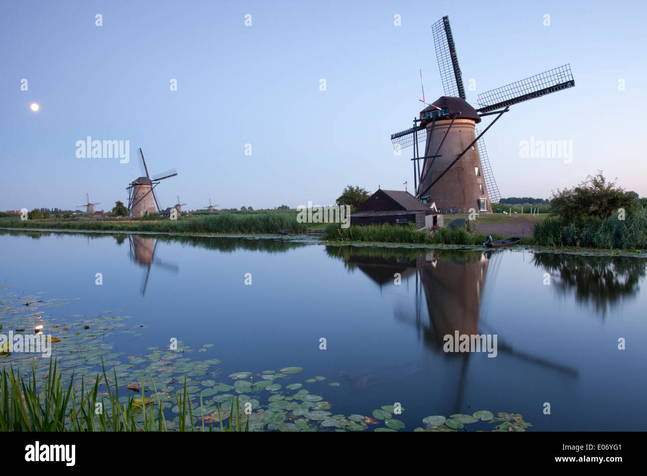 View of two windmills and their reflections in the surrounding polder waters at sunset, Kinderdijk, Nieuw-Lekkerland, Holland. Stock Photo