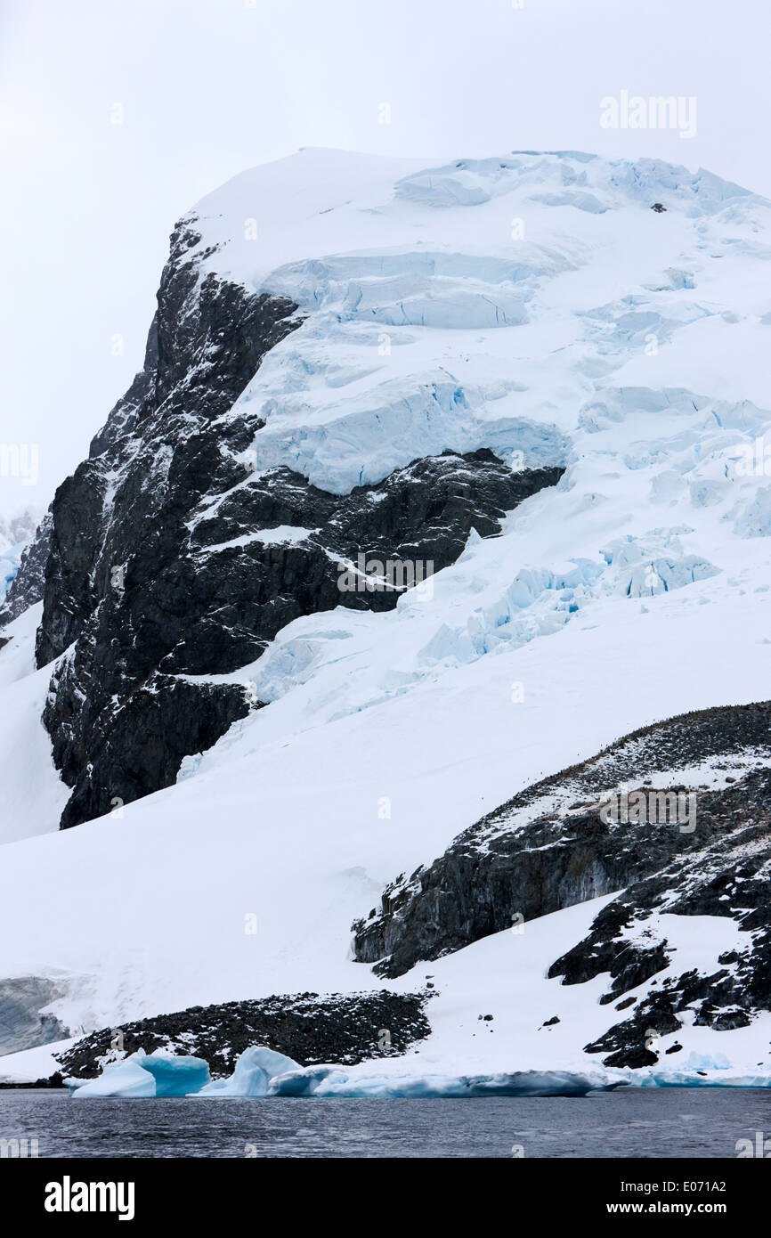 snow and ice capped mountains and glacier with penguin colony on cuverville island antarctica Stock Photo