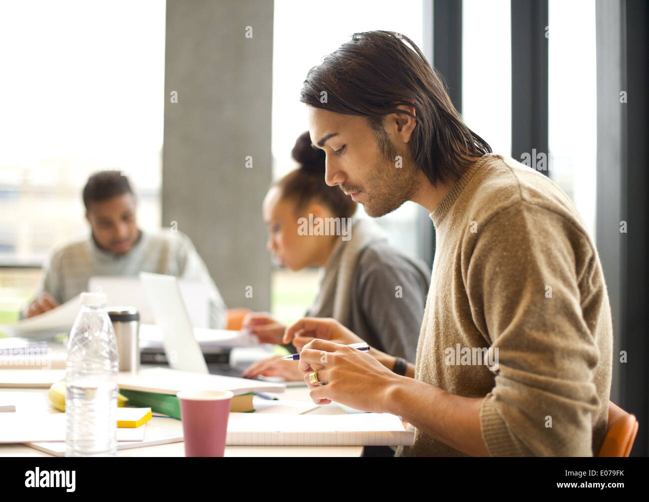 Young man talking notes for study with students studying in background. University students preparing for final exams in library Stock Photo