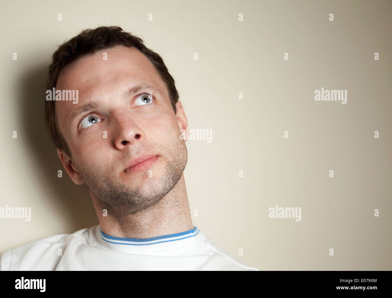Thinking young Caucasian man in white t-shirt. Closeup portrait Stock Photo