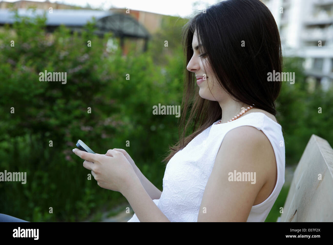 Side view portrait of a woman sitting on the outdoor bench and typing on the phone Stock Photo