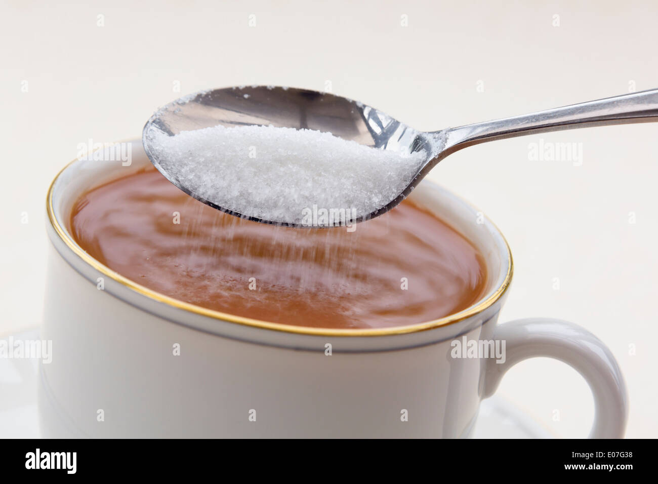 Adding a spoon of white granulated sugar into a cup of tea in a teacup can contribute to diabetes and extra calories weight gain. England UK Stock Photo