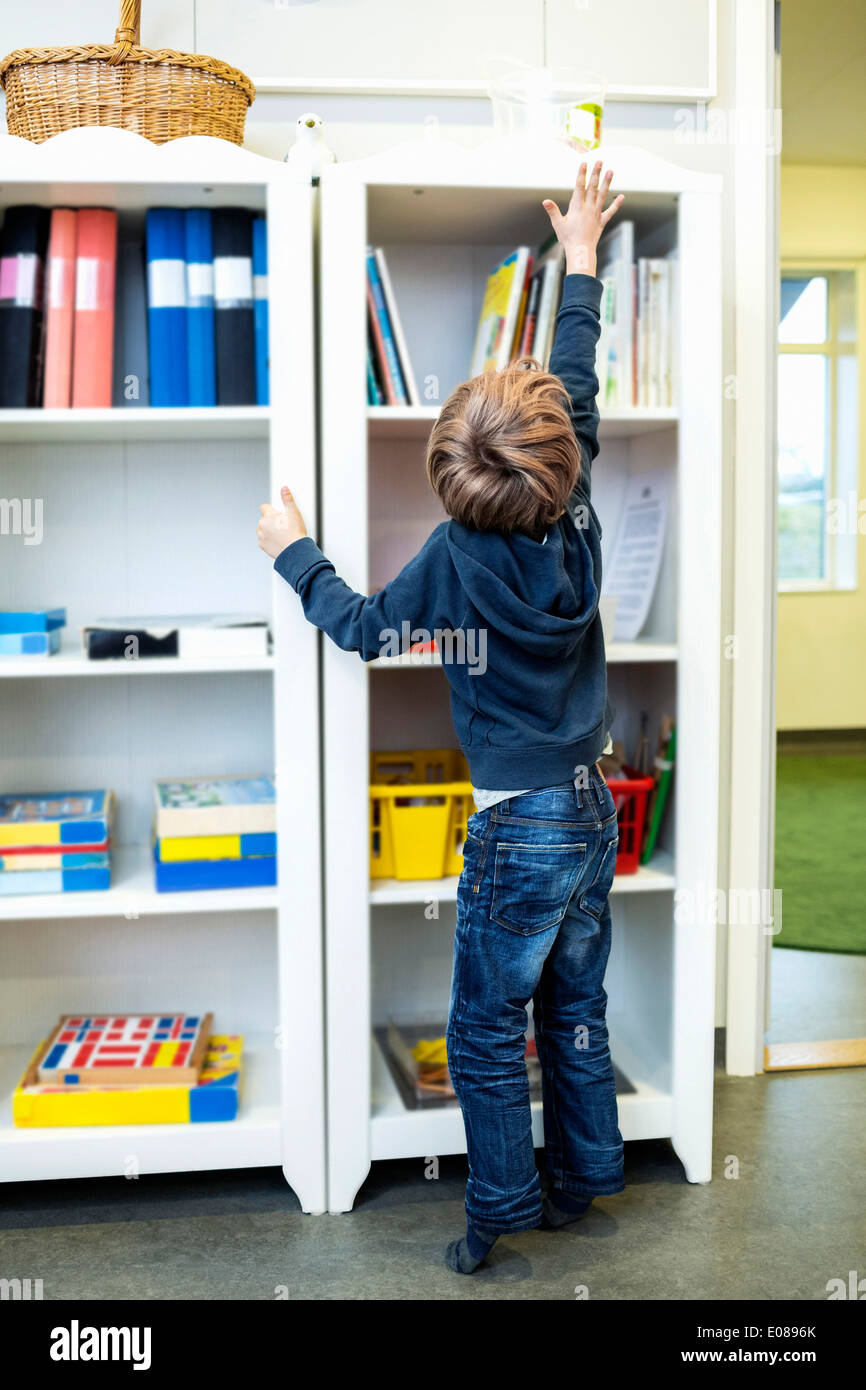 Rear view of boy reaching for container on shelf in kindergarten Stock Photo