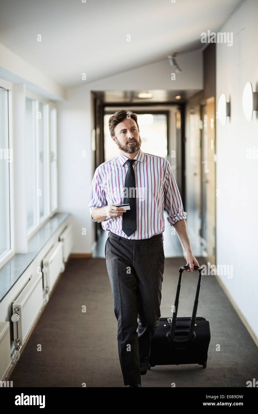 Businessman with suitcase walking in hotel corridor Stock Photo