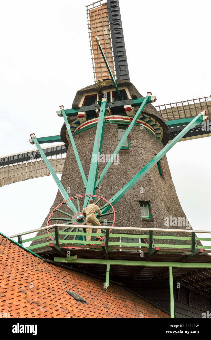 DUTCH WINDMILL WITH MAN ROTATING THE WHEEL TO ADJUST THE PITCH OF THE SAILS ZAANSE SCHANS HOLLAND Stock Photo