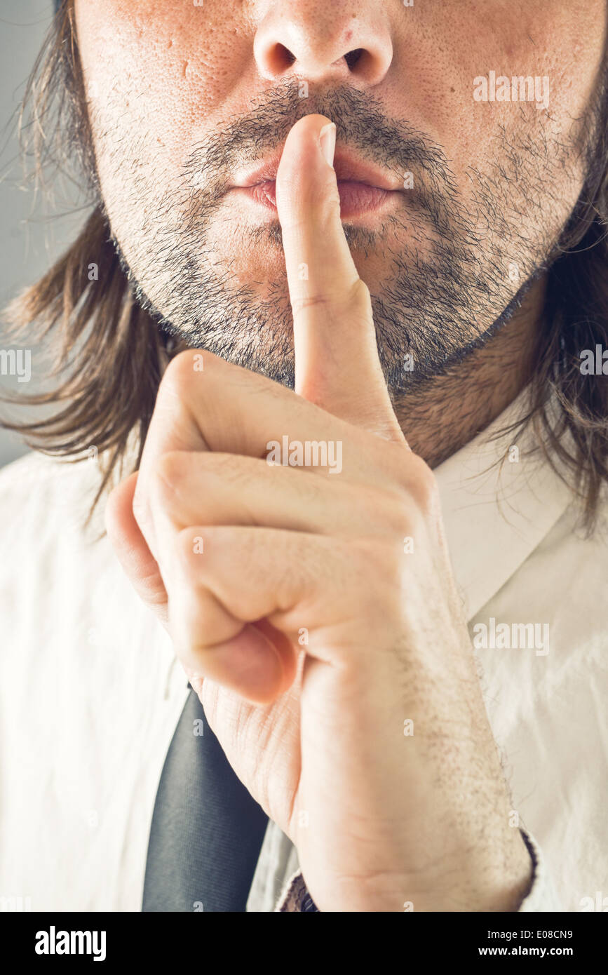 Businessman making hush gesture, finger on mouth for silence. Stock Photo