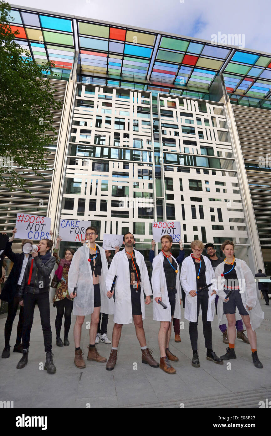 London, UK. 6th May 2014. Act Up Docs not Cops Immigration Bill protest at the Home Office in London with protestors dressed as doctors stripping off to become police. ACT UP London is fighting against two clauses in the Immigration Bill, which will serve to introduce charges for health services, turn doctors into border agents, and increase HIV infection. Credit:  Paul Brown/Alamy Live News Stock Photo