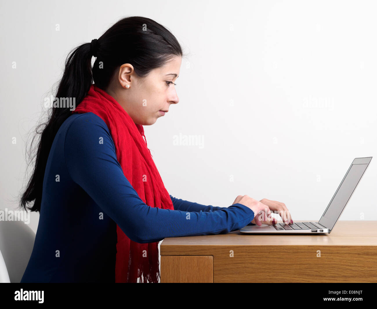 Side view of a young woman using a laptop computer on a wooden desk Stock Photo