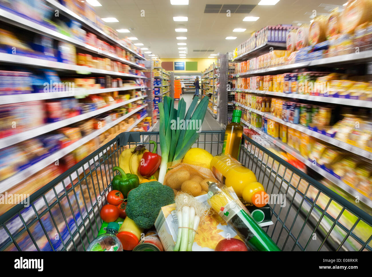 Shopping cart with foods between store shelves in a supermarket. Stock Photo