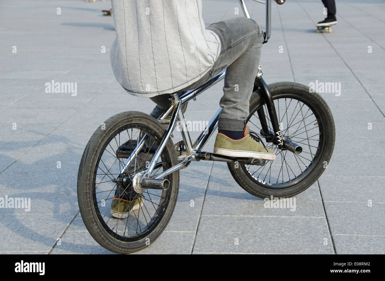 fragment of guy with sports clothing sit on sports BMX bicycle on grey urban concrete background Stock Photo