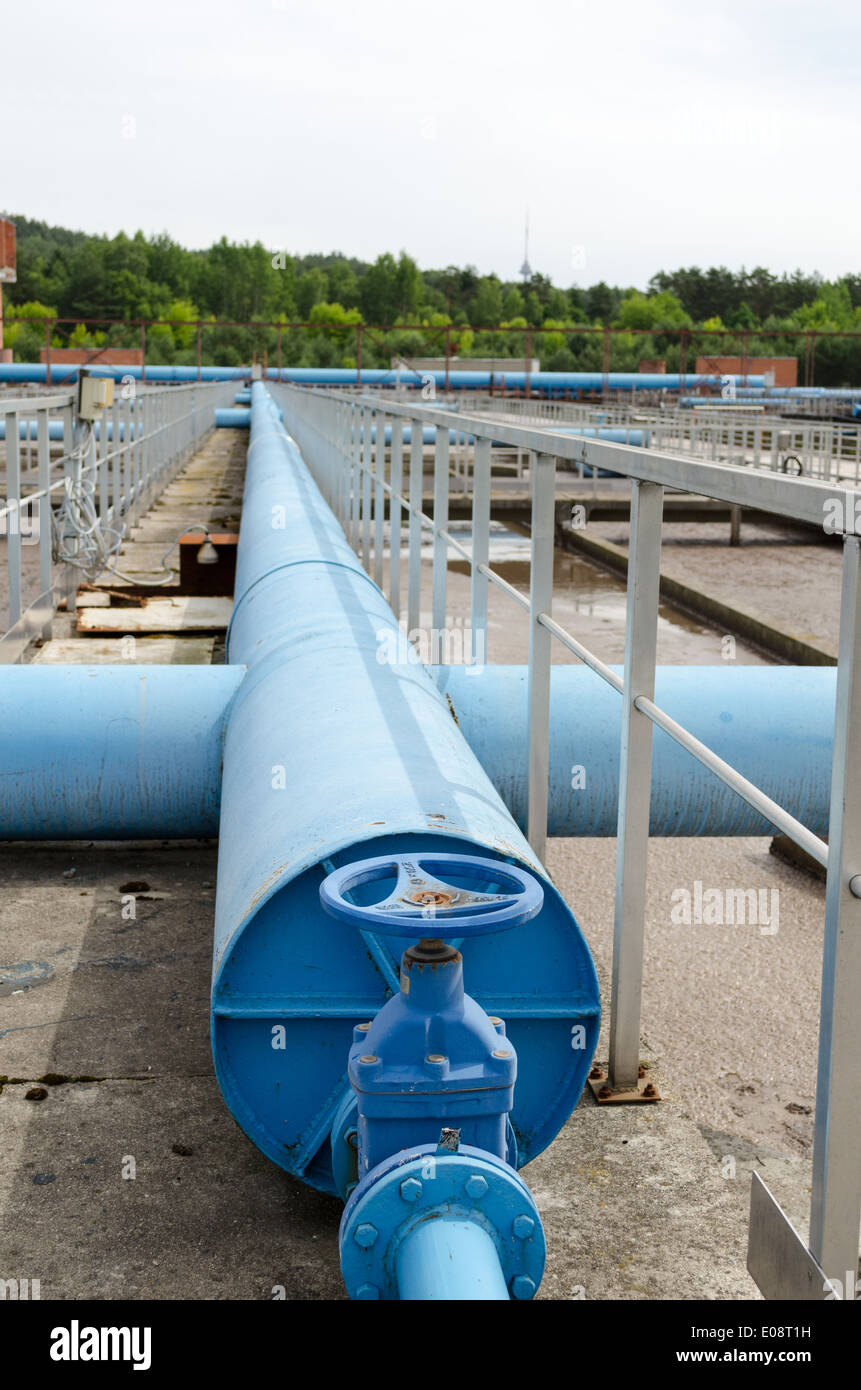 Blue stopcock tap valve gate and pipes in water treatment plant and dirty liquid bubble in background. Stock Photo