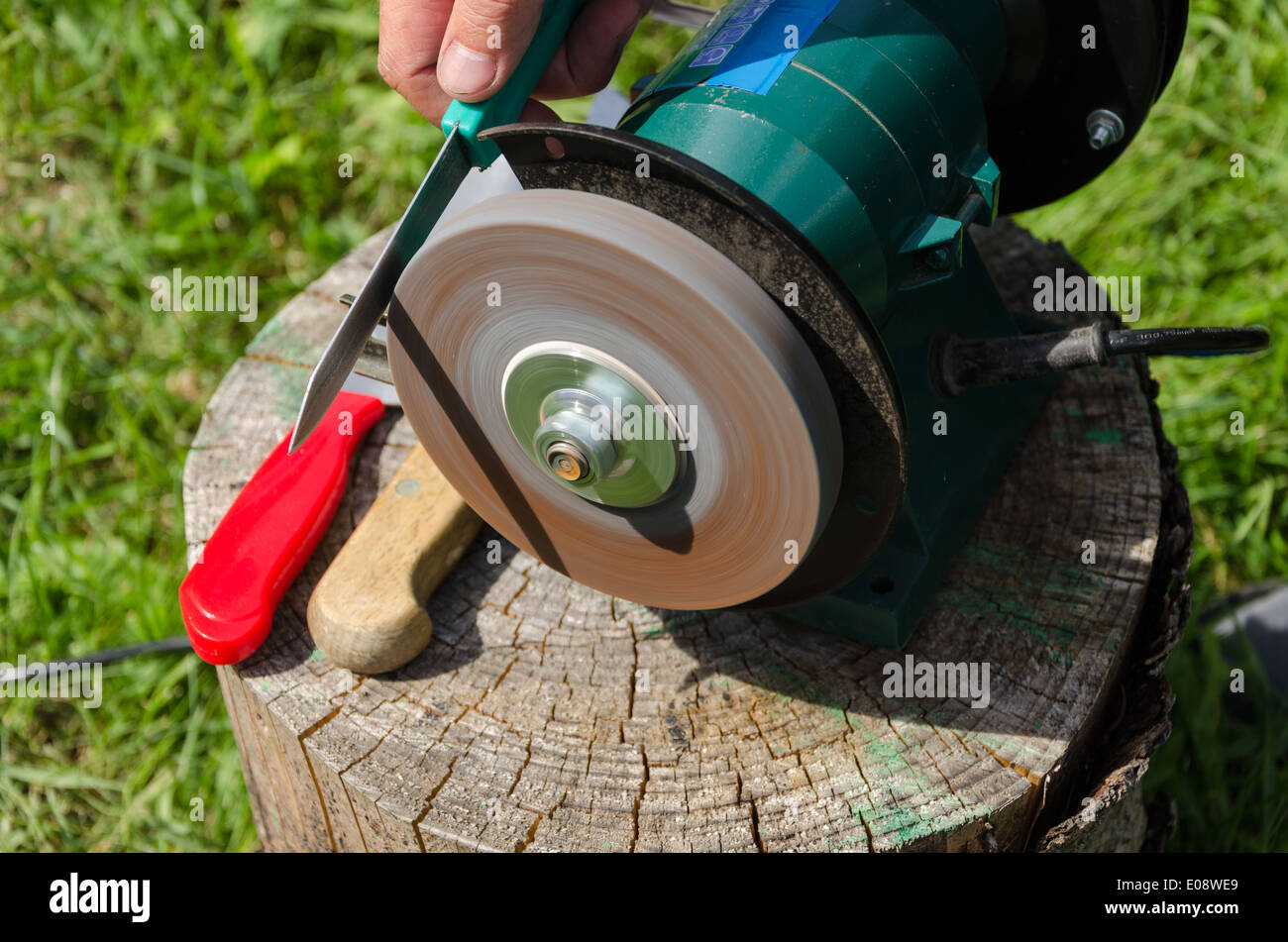 Hand sharpening knives with electric grinder tool on outdoor wood log. Stock Photo