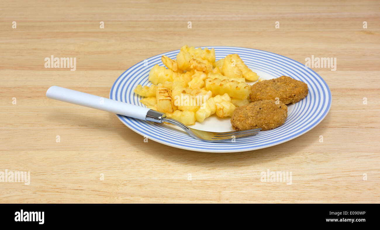 A plate of chicken nuggets with french fries and fork on a dining table. Stock Photo