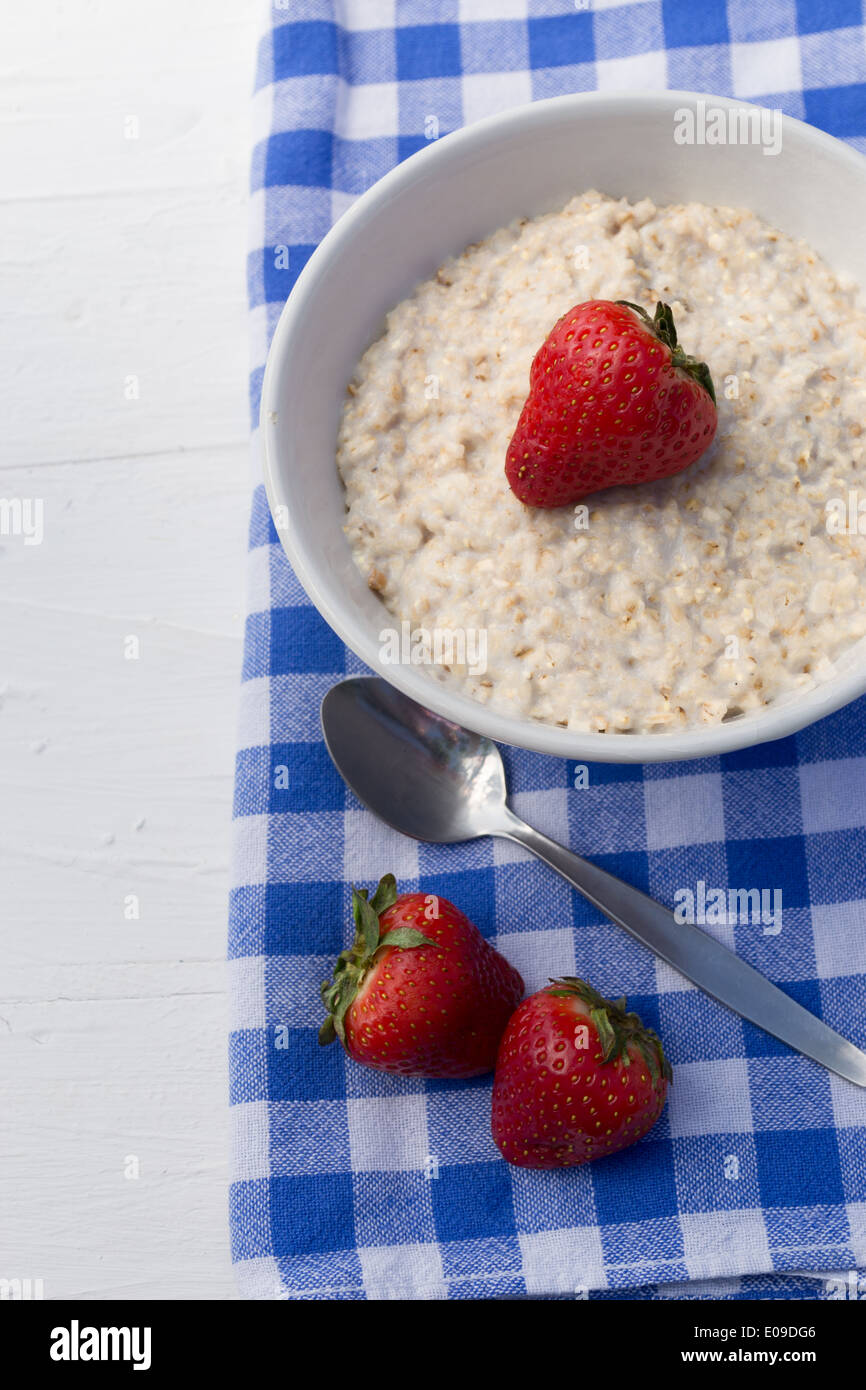Strawberries and porridge in a bowl on a white table with a blue and white checkered tea towel