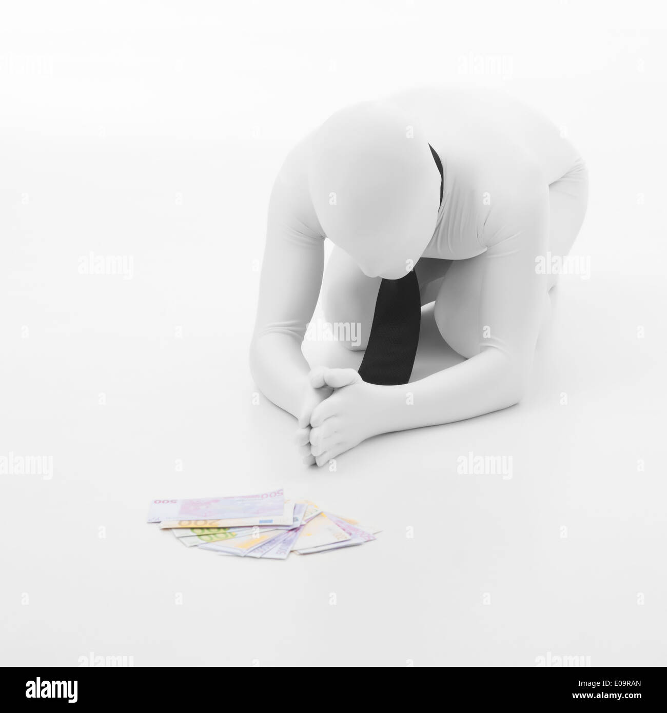 man dressed in white with black tie prays to money, standing on his knees, on white background Stock Photo