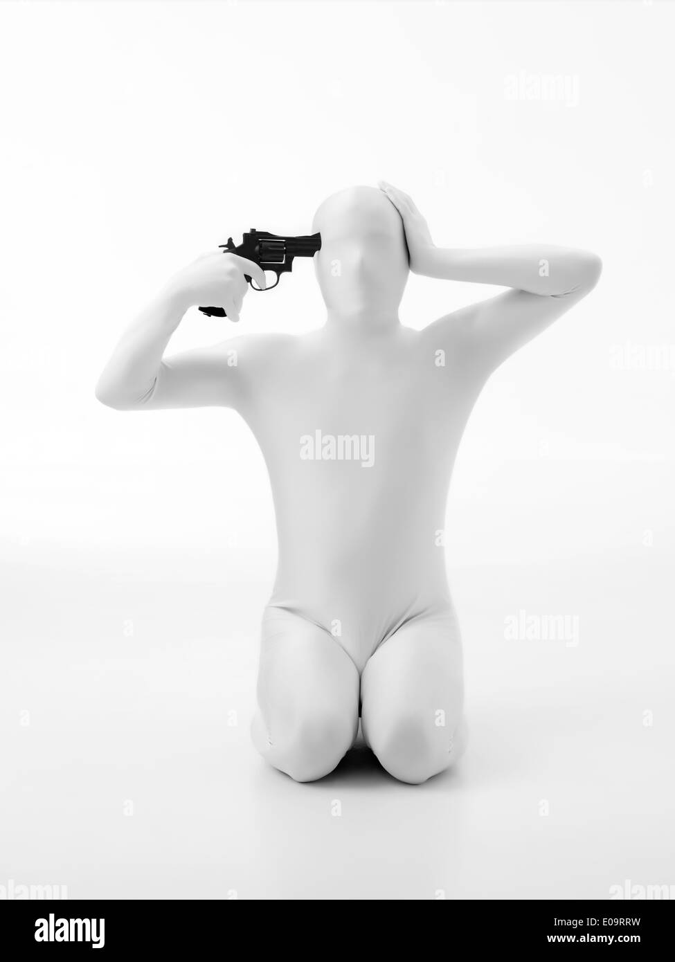 faceless man dressed in white, sitting on his knees, holding gun against his head Stock Photo