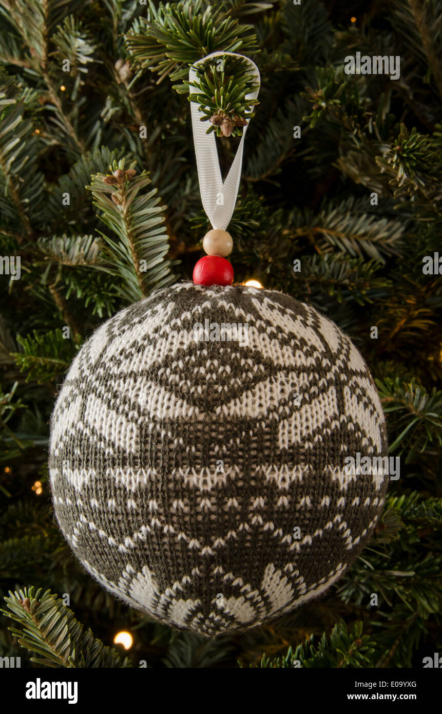 White and gray knit ornament hangs on a gently lit Christmas fir tree Stock Photo