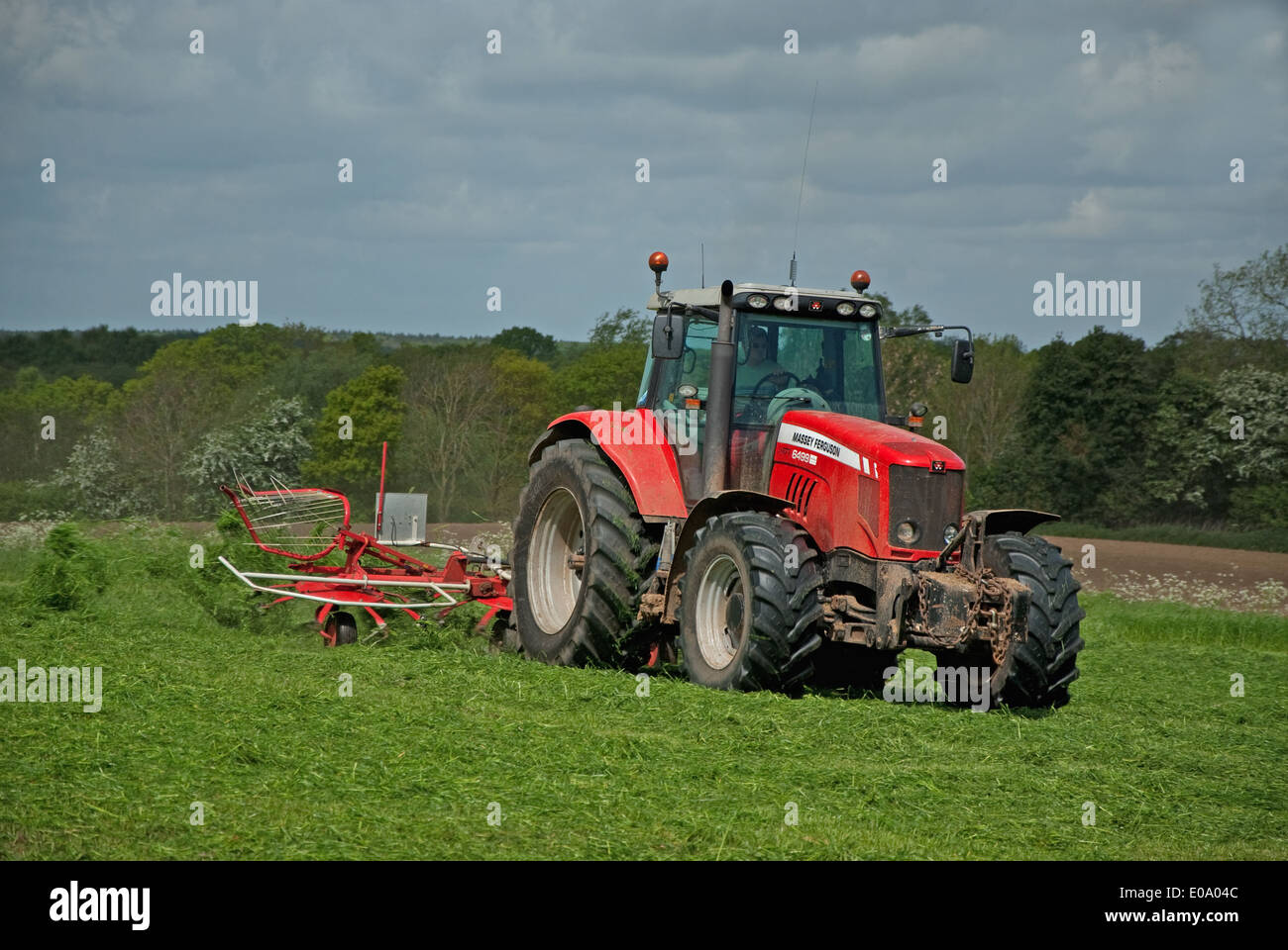 Tractor turning grass to dry for silage in British countryside in spring Stock Photo