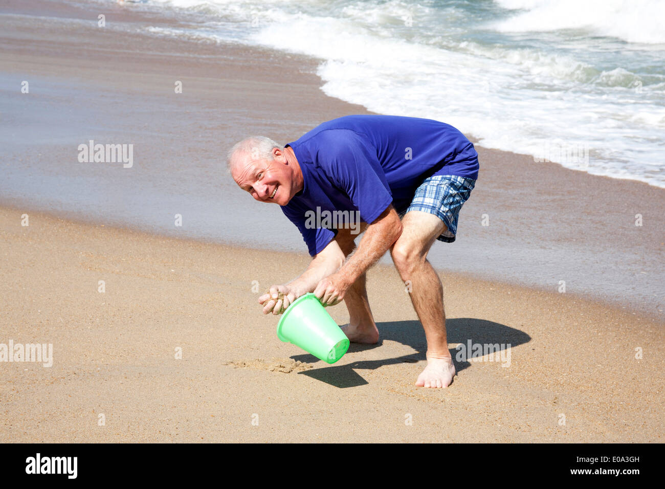 Man collecting sand in a pail while acting childish at the shore Stock Photo