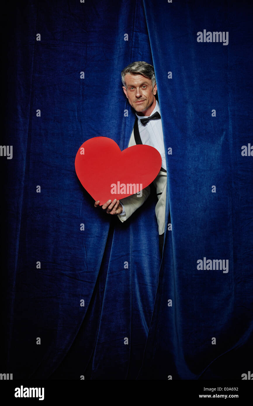 Man behind curtain with big red paper heart Stock Photo