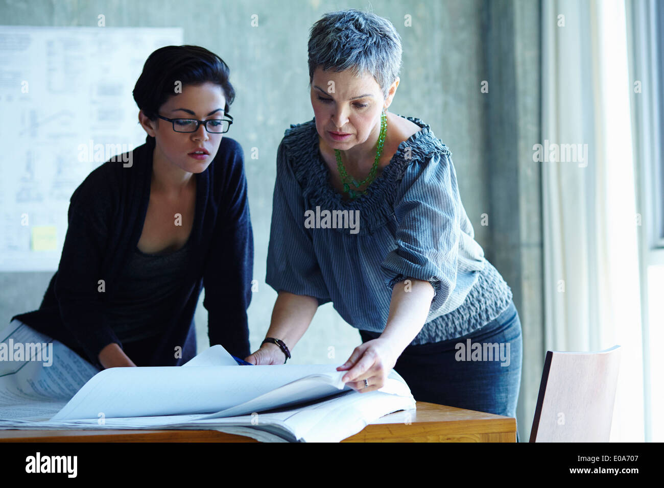 Two businesswomen checking blue prints in office Stock Photo