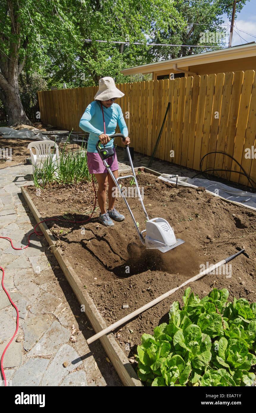 a woman rototilling her garden in the spring with an electric rototiller Stock Photo