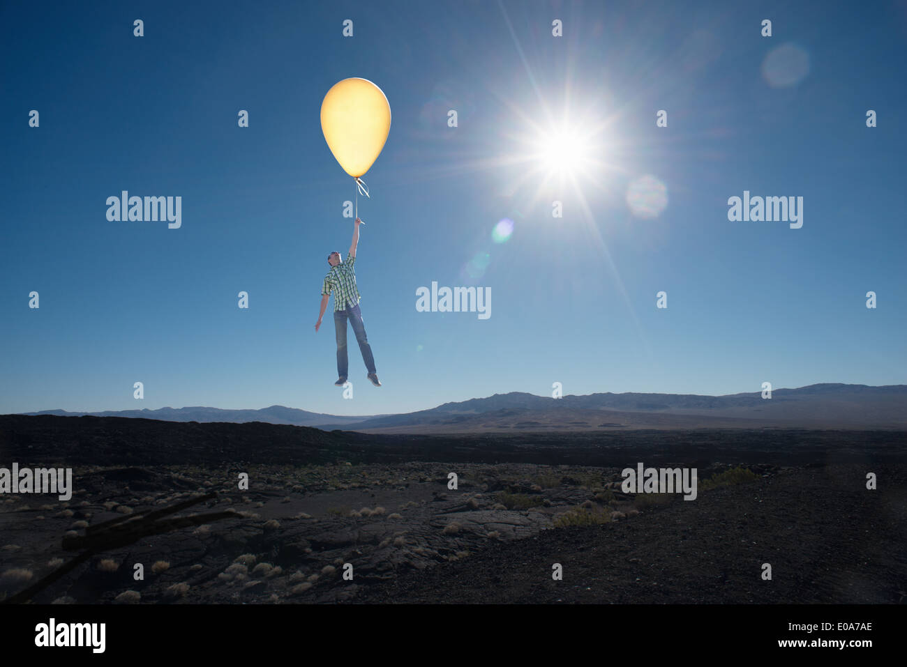 Mid adult man floating with balloon in desert Stock Photo
