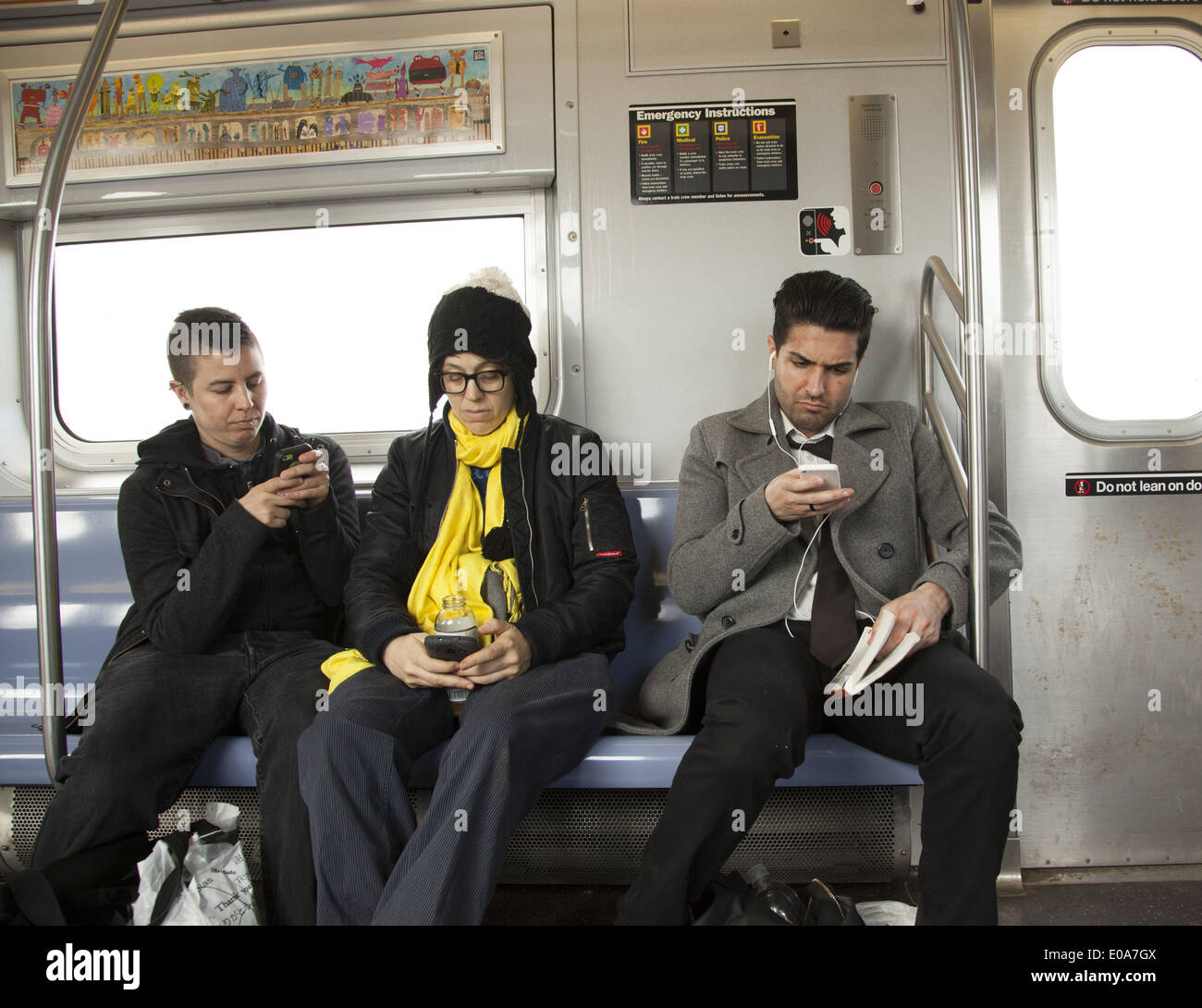 Riders check their smartphones when the subway goes above ground in Brooklyn along the F line. Stock Photo