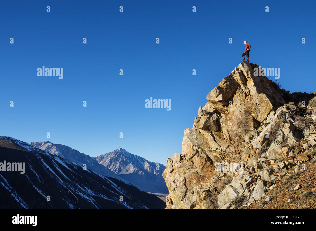 man on rocky peak looking across valley at distant mountains Stock Photo