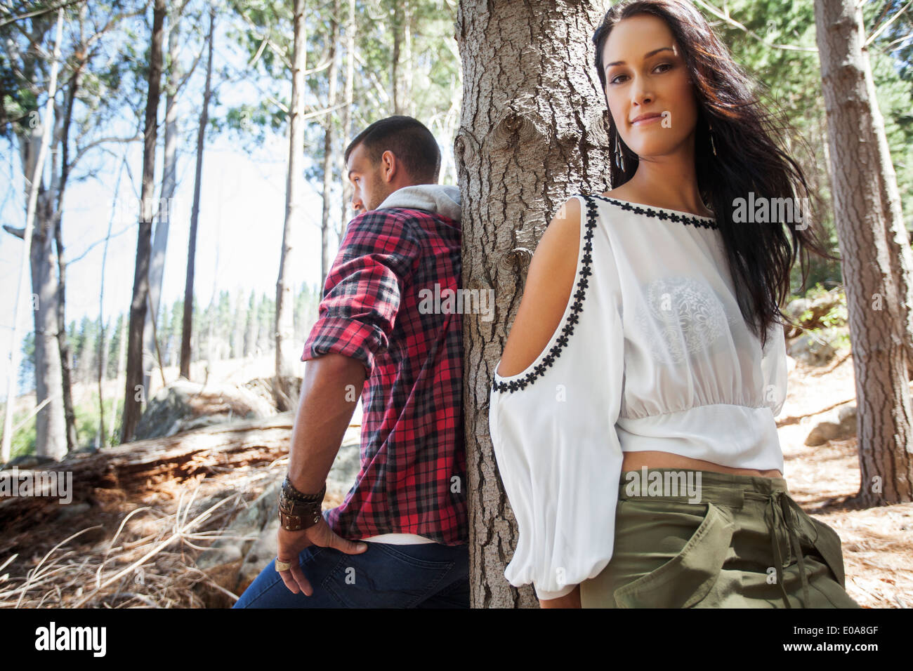 Young couple leaning against tree in forest Stock Photo