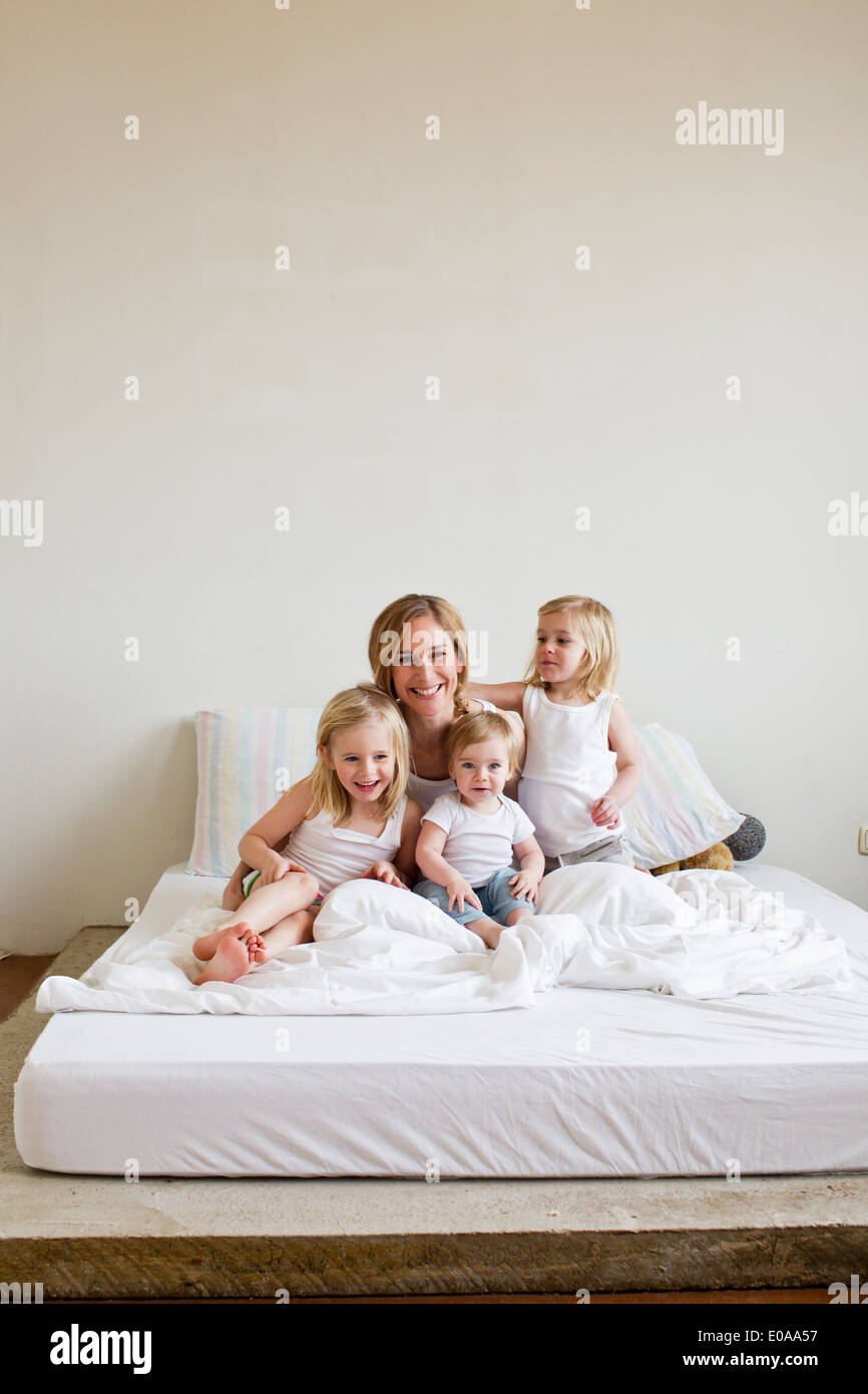 Portrait of mid adult woman in bed with three daughters Stock Photo
