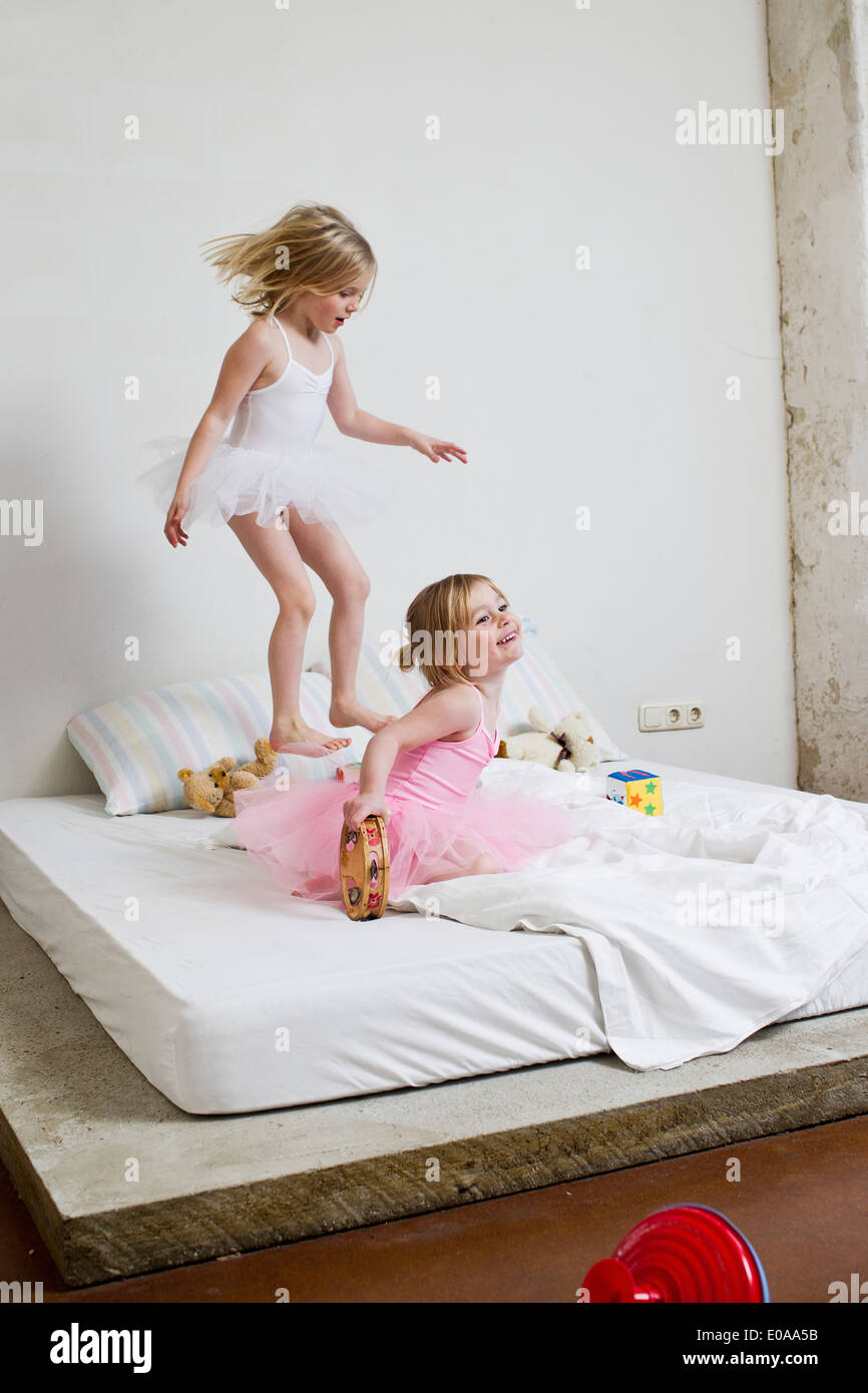 Two young sisters dressed as ballet dancers playing on bed Stock Photo