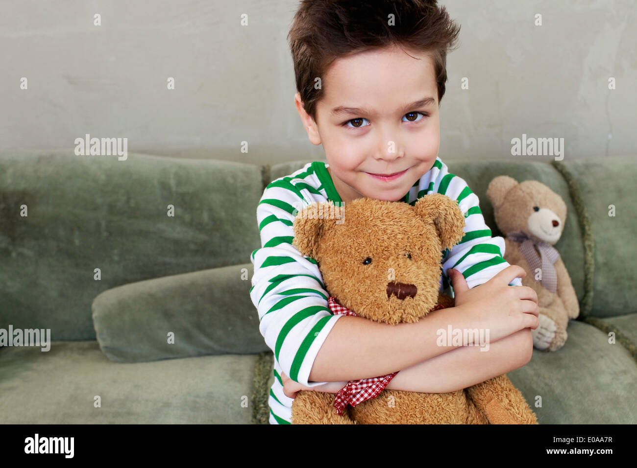 Portrait of young boy on sofa hugging teddy Stock Photo