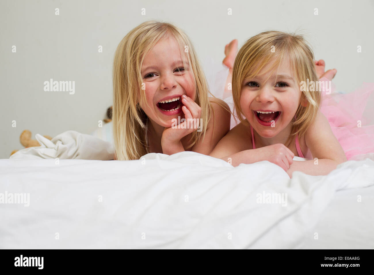 Portrait of two young sisters lying on front in bed Stock Photo