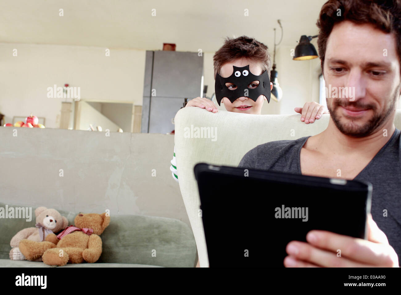 Masked son distracting father from digital tablet Stock Photo