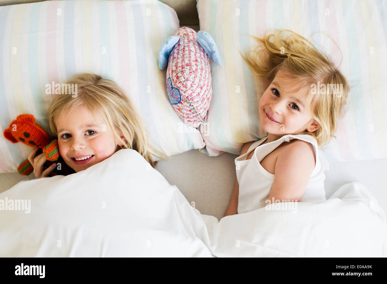 Portrait of two young sisters lying side by side in bed Stock Photo