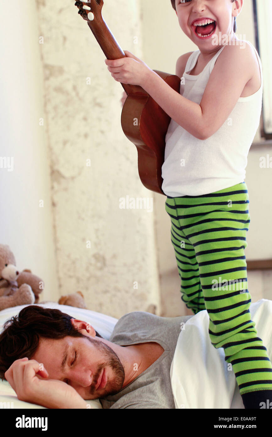 Son playing guitar whilst his father sleeps Stock Photo