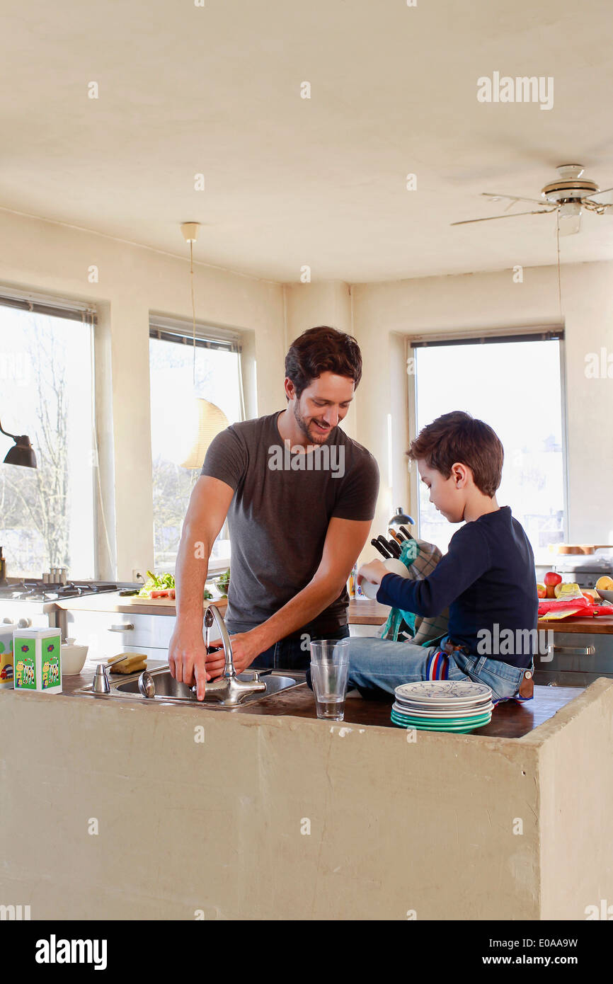 Father and young son clearing up in kitchen Stock Photo