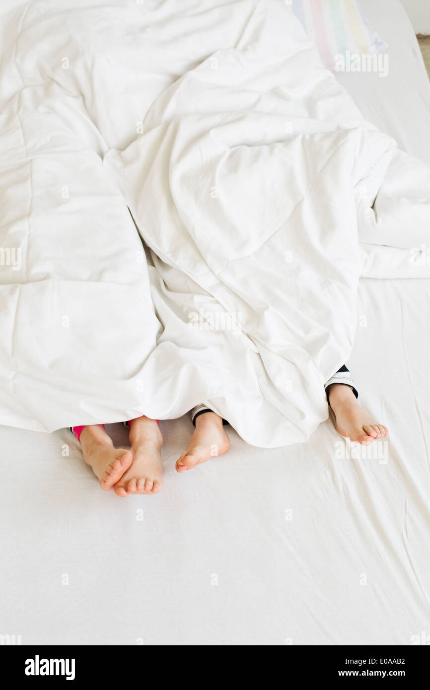 Young sisters feet sticking out of duvet on bed Stock Photo