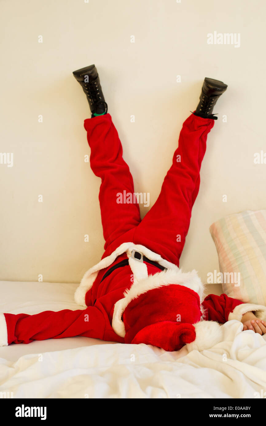Young boy dressed up as santa claus on bed with legs raised Stock Photo