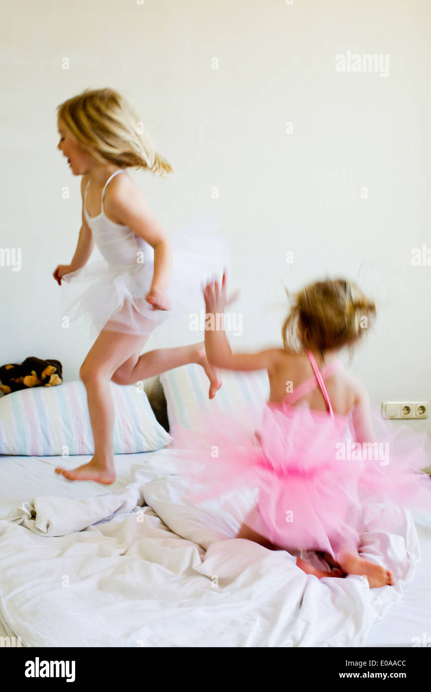 Sisters dressed as ballet dancers running on bed Stock Photo