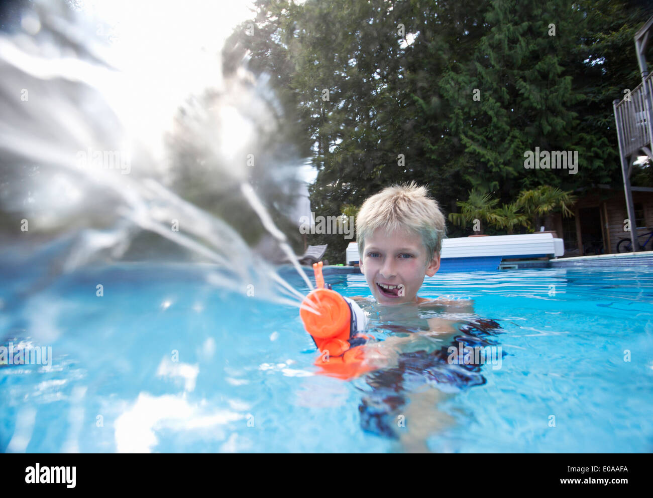Boy in swimming pool squirting water gun Stock Photo