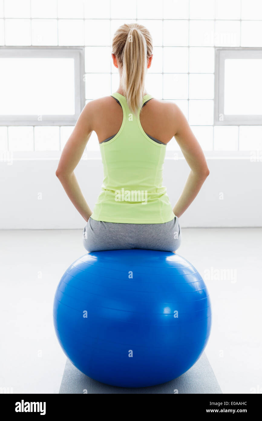 Young woman sitting on exercise ball, rear view Stock Photo