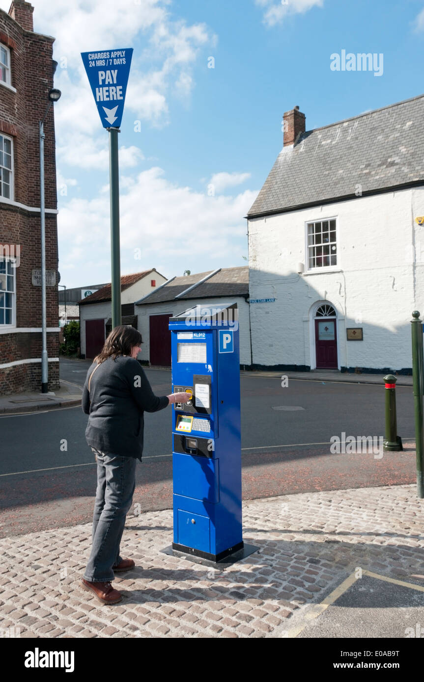 Woman purchasing a car park ticket from a machine on the Tuesday Market Place, King's Lynn, Norfolk. Stock Photo