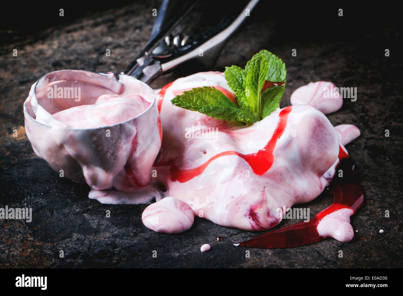 Close up of melting strawberry ice cream with fresh mint and metal spoon over black table. Stock Photo