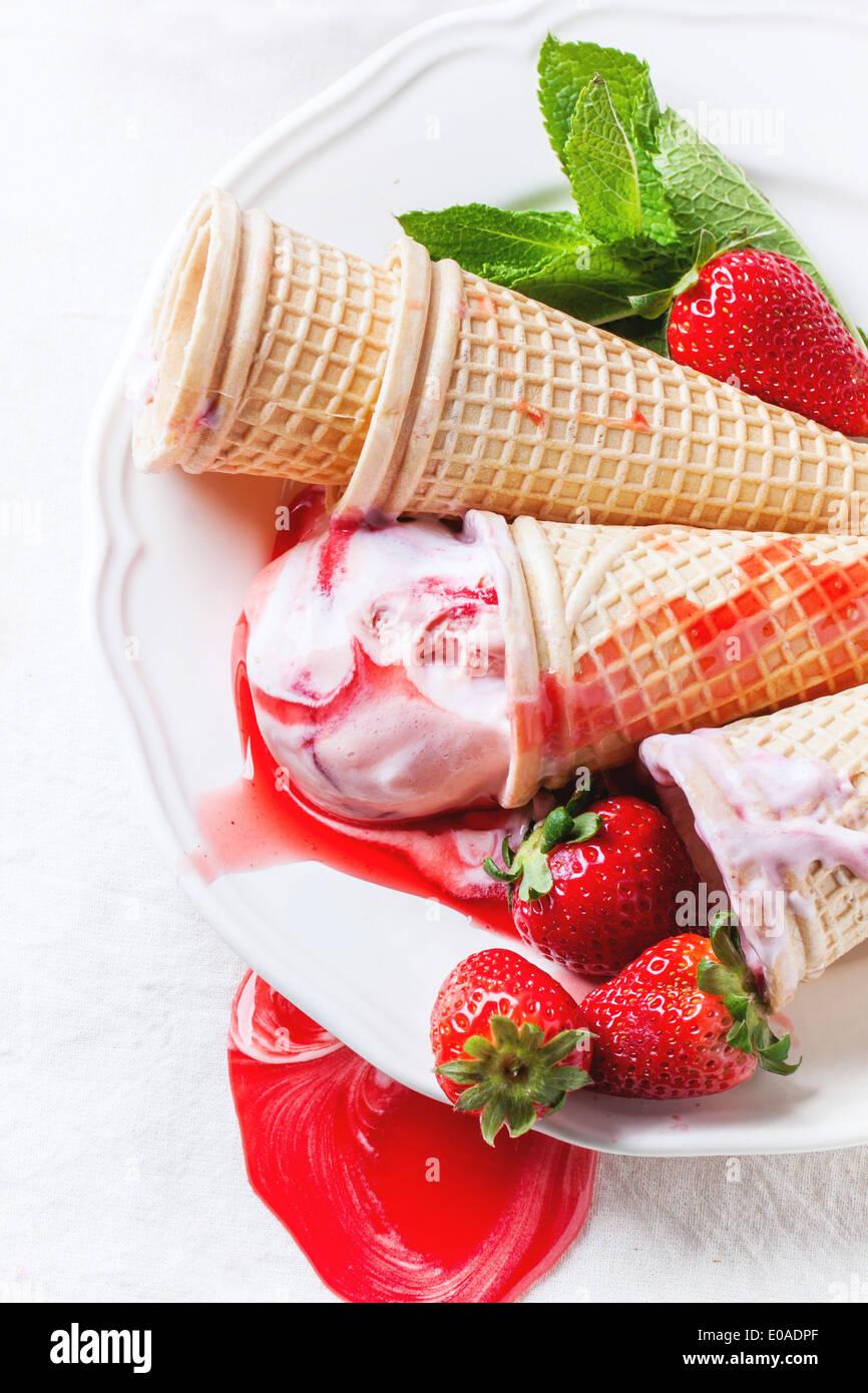 Wafer cones with strawberry ice cream with syrup, mint and fresh strawberries served on white plate. Stock Photo